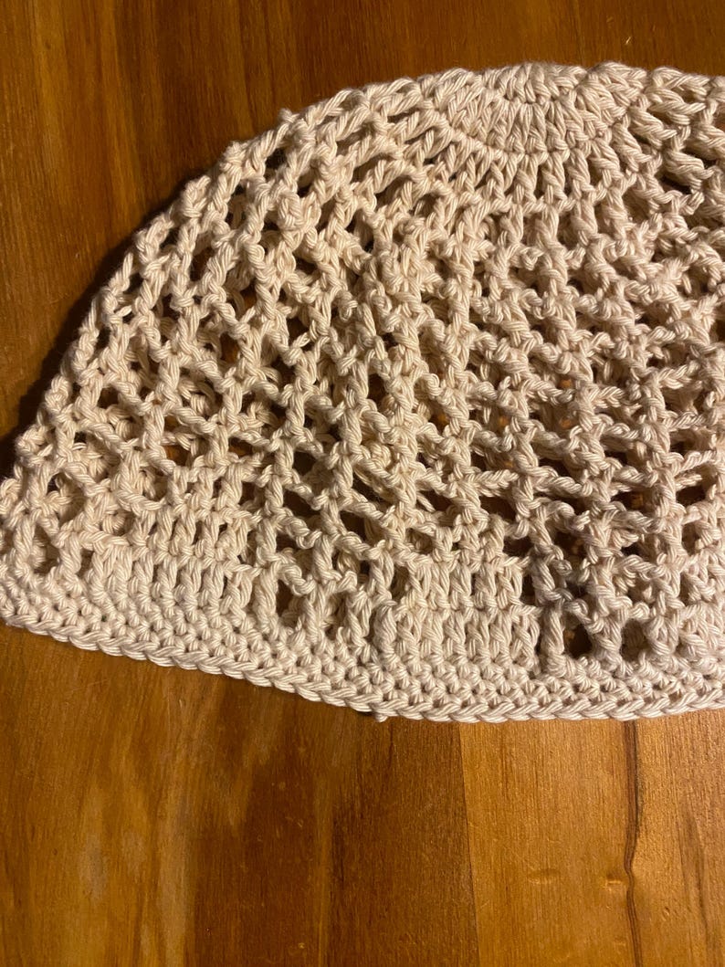 May include: A beige crocheted hat with a delicate openwork pattern. The hat is made with a soft, lightweight yarn and has a comfortable fit.