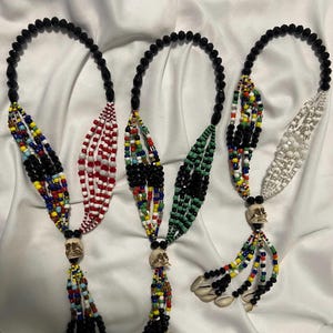 May include: Three beaded necklaces with skull charms and shell accents. Each necklace features a different colour scheme: red, white and black; green, white and black; and white and black.