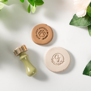 Peut inclure: Ensemble d'outils et de tampons de poterie. Comprend un outil à manche vert clair avec un dessus doré, un tampon beige avec une empreinte de patte et un tampon beige avec les lettres "CL" dans une couronne. Le tampon de patte indique "Purr-fect Pottery by Momo."