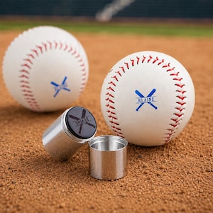 May include: Two white baseballs with red stitching and a blue graphic of crossed bats with the text BLAINE, alongside a small, two-piece cylindrical metal container with a black lid featuring a black graphic of crossed bats and the text BLAINE.
