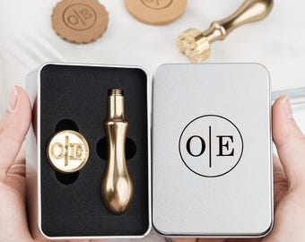 Puede incluir: Un juego de sellos de lacre de color dorado con las iniciales "O|E" dentro de una lata plateada. El juego incluye un sello, un mango y dos sellos de cera. La tapa de la lata también presenta las iniciales "O|E".