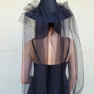 May include: Black witch hat with a tall, pointed crown and a wide brim. The hat is adorned with a black tulle veil that drapes down the back. The hat is part of a Halloween costume.