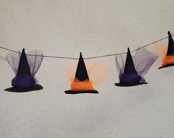 May include: A decorative garland featuring four miniature black witch hats suspended on a thin black string. Each hat is accented with either vibrant orange or deep purple tulle fabric wrapped around the base, creating a festive Halloween display.