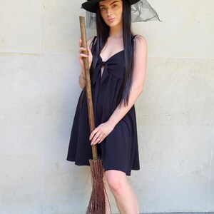 May include: A black witch hat with gold accents and a sheer veil, paired with a black dress and a broom. The hat features a crescent moon and star design. The broom is made of wooden handle and twigs.