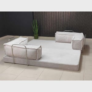 Pu&ograve; includere: Un set di divani modulari in velluto a coste di colore chiaro. Il set comprende una grande base rettangolare e diversi componenti quadrati imbottiti con telai in metallo. Il divano &egrave; progettato per composizioni versatili e sedute confortevoli.