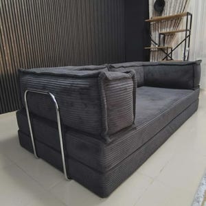 Peut inclure: Un canap&eacute; en velours c&ocirc;tel&eacute; gris avec un design modulaire. Le canap&eacute; a un profil bas et une esth&eacute;tique simple et moderne. Il est dot&eacute; d'un cadre en m&eacute;tal et convient &agrave; un salon ou un coin salon.