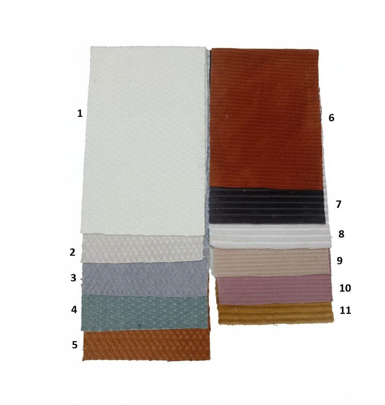 May include: Eleven fabric swatches in a variety of colours and textures are displayed. The swatches include white, grey, blue, and brown tones, with a mix of smooth and textured surfaces. The arrangement showcases a range of materials for design and crafting.