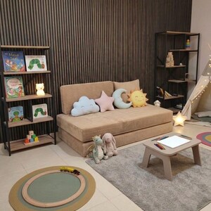 May include: A child's playroom with a beige sofa, decorative pillows, and a small table with crayons. A rug with a train track and a bookshelf with books and a bear-shaped nightlight are also visible.