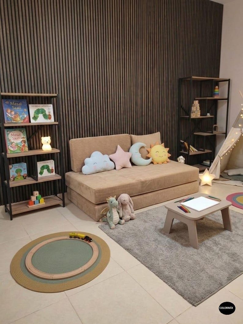May include: A child's playroom with a beige sofa, decorative pillows, and a small table with crayons. A rug with a train track and a bookshelf with books and a bear-shaped nightlight are also visible.