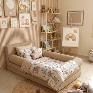 May include: A child's bedroom with a beige bed, a round woven rug, and a wooden bookshelf. The bed has a patterned quilt and pillows. Artwork with animal illustrations and a rainbow painting adorn the walls. Toys and books are arranged throughout the room.