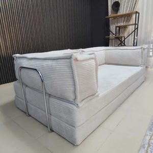 Pu&ograve; includere: Un divano color crema con texture a coste, a basso profilo e dal design minimalista. Il divano presenta una struttura in metallo e cuscini morbidi, offrendo un'estetica moderna. Progettato per il comfort e il relax.