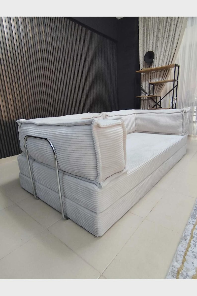 Pu&ograve; includere: Un divano color crema con texture a coste, a basso profilo e dal design minimalista. Il divano presenta una struttura in metallo e cuscini morbidi, offrendo un'estetica moderna. Progettato per il comfort e il relax.