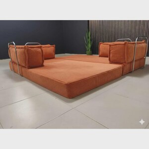 May include: An orange modular sofa with a low profile and a corduroy texture. The sofa has a rectangular base and two sections with square cushions and metal frames. The design is modern and minimalist.