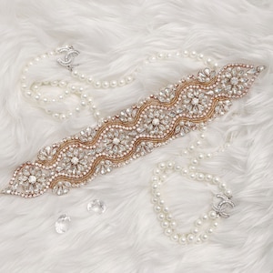 May include: A delicate gold-toned rhinestone belt with a floral design, paired with a double strand of white pearl necklaces and a pearl bracelet with a silver clasp.