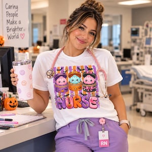 Puede incluir: Una camiseta blanca con un gráfico de tres adorables y coloridas empanadillas en cestas de bambú, rodeadas de murciélagos y la palabra NURSE en letras moradas. El diseño incluye rayas naranjas y moradas, estrellas y pequeñas calabazas.