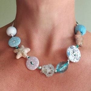 May include: A necklace made with white, blue, and green beads, buttons, and a starfish charm.