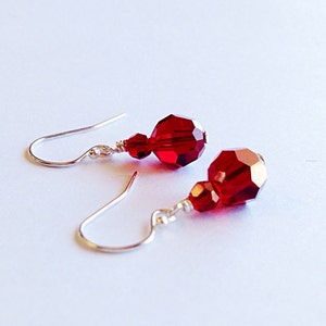 May include: A pair of silver dangle earrings with two red crystal beads on each earring.