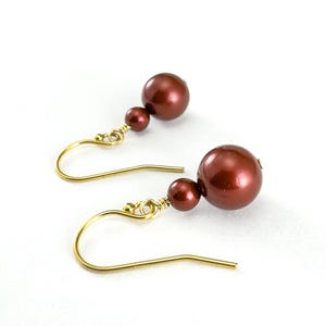 Op de afbeelding: Een paar oorhangers met kastanjebruine, bolvormige kralen en goudkleurige oorhaken. De oorbellen hebben een klassiek, elegant ontwerp, geschikt voor diverse gelegenheden. De kralen zijn ongeveer 1 cm in diameter.