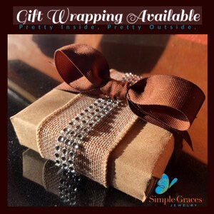 Pode incluir: Uma caixa de presente marrom embrulhada em fita de juta com um la&ccedil;o marrom e strass prateados. A caixa est&aacute; sobre uma superf&iacute;cie preta. O texto "Gift Wrapping Available" est&aacute; na parte superior da imagem. O texto "Pretty Inside. Pretty Outside." est&aacute; abaixo da primeira linha de texto. O texto "Simple Graces Jewelry" est&aacute; na parte inferior da imagem.