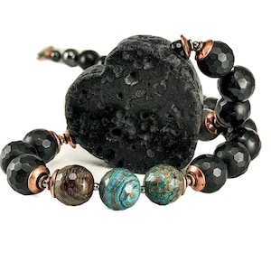 Könnte beinhalten: Ein Perlenarmband mit einem großen, strukturierten schwarzen herzförmigen Stein. Das Armband enthält facettierte schwarze Perlen, kupferfarbene Akzente und eine Mischung aus braunen und türkisfarbenen runden Perlen. Das Armband befindet sich auf weißem Hintergrund.