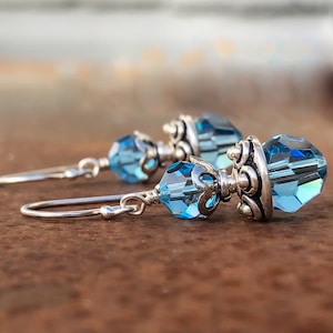 May include: A pair of silver dangle earrings with a light blue crystal teardrop pendant. The crystal is faceted and has a silver setting.