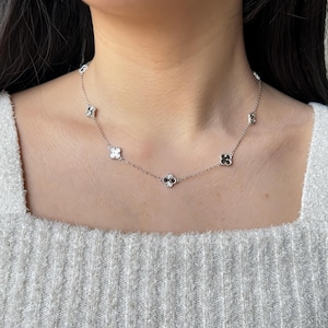 May include: A delicate silver necklace featuring multiple clover-shaped pendants. The necklace is displayed on a person's neck, showcasing the intricate design and the way it lays. The clover pendants are evenly spaced along the chain.