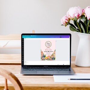 K&ouml;nnte beinhalten: Ein Laptop-Computer, auf dem eine digitale Einladung mit rosa Hintergrund und einem Blumenkranz angezeigt wird. Der Einladungstext lautet "There's a village in my belly" und "Baby Shower for Rosie Smith".