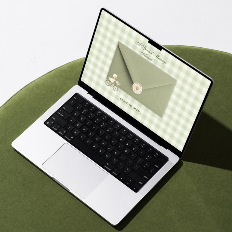 Laptop on a green surface displaying the sage gingham click-to-open envelope page of the Silly Goose baby shower website template.
