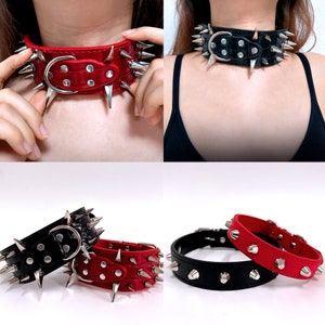 K&ouml;nnte beinhalten: Zwei mit Spikes besetzte Lederhalsb&auml;nder, eines rot und eines schwarz. Beide Halsb&auml;nder haben silberne Metallakzente und Spikes.