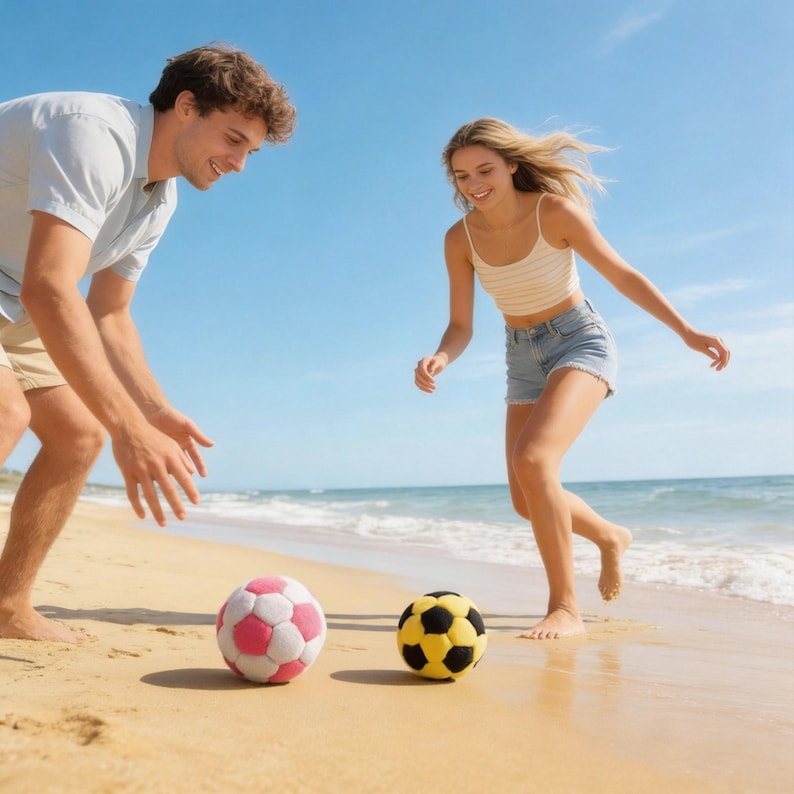 May include: Two soccer balls, one pink and white, the other yellow and black, sit on a sandy beach. A person in a light blue shirt and shorts is about to kick the pink ball. Another person in a white and tan striped top and denim shorts is running towards the yellow ball.
