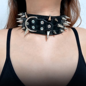 K&ouml;nnte beinhalten: Ein schwarzer Leder-Choker mit silbernen Spikes. Der Choker hat einen Schnallenverschluss.