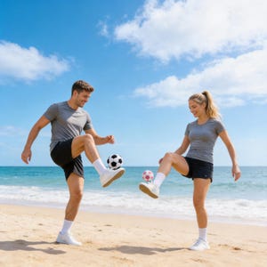 May include: Two people playing soccer on a sandy beach. They are wearing gray shirts, black shorts, and white sneakers. One soccer ball is black and white, and the other is pink and white. The sky is blue with white clouds, and the ocean is visible in the background.