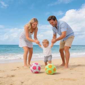 May include: A family enjoys a day at the beach with a toddler. Two colorful soccer balls, one pink and white, the other green and orange, sit on the sand. The sky is blue with a few clouds, and the ocean waves are visible in the background.