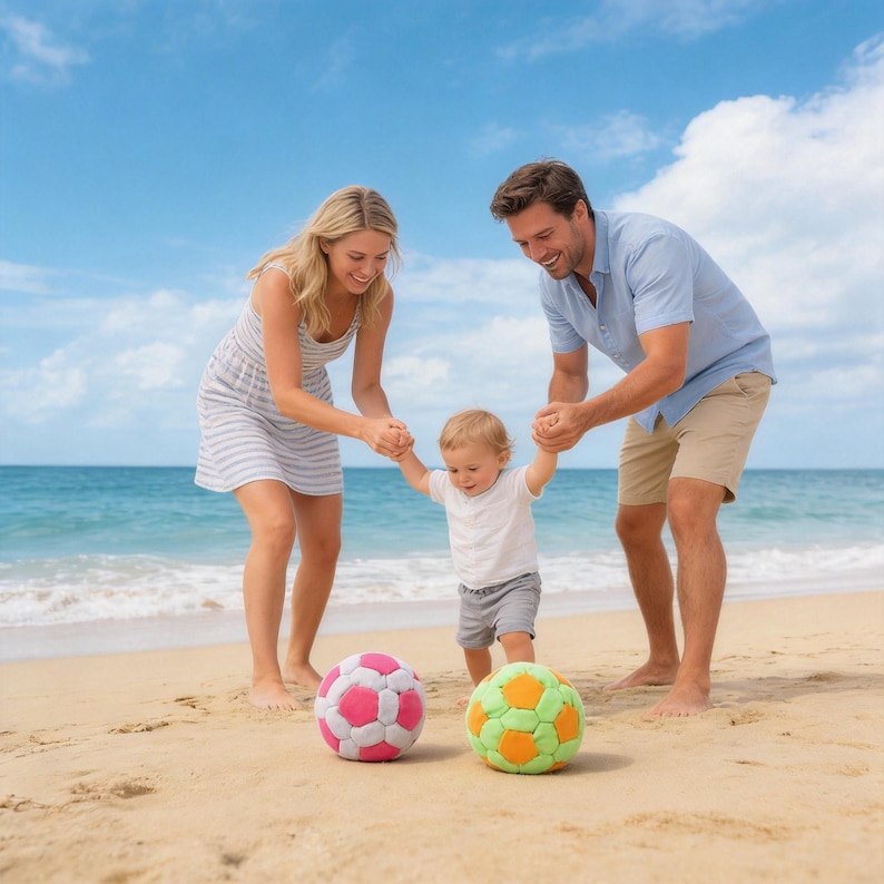 May include: A family enjoys a day at the beach with a toddler. Two colorful soccer balls, one pink and white, the other green and orange, sit on the sand. The sky is blue with a few clouds, and the ocean waves are visible in the background.