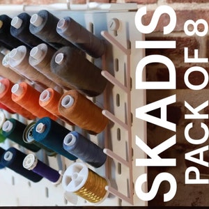 May include: A white plastic thread organiser with eight slots, labelled "SKADIS PACK OF 8". The organiser is filled with spools of colourful thread.