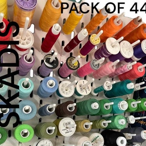 May include: A pack of 44 colourful spools of thread organised on a white pegboard. The pegboard is labelled "SKADIS" and "PACK OF 44".