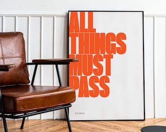 May include: A framed poster with the text "ALL THINGS MUST PASS" in orange letters on a white background. The poster is hanging on a white wall next to a brown leather armchair and a black floor lamp.