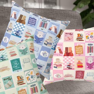 Könnte beinhalten: Drei dekorative Zierkissen mit einem Buch-Thema. Jedes Kissen hat ein sich wiederholendes Muster aus Büchern, Kaffeetassen und Lese-Illustrationen in Pastellfarben. Die Kissen haben den Text "Read up!" und "Explore Dream Read".