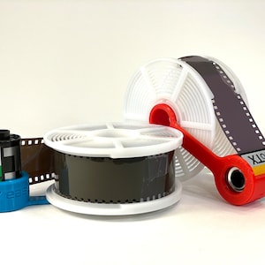 Puede incluir: Dos carretes de revelado de película de plástico blanco con un soporte de líder de película de plástico rojo y un bote de película negro y amarillo etiquetado "400TX" y "Kodak".