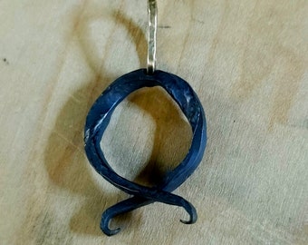 May include: A black metal pendant in the shape of a stylized letter Q with a gold jump ring at the top.