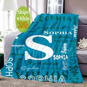 May include: A bright blue fleece blanket featuring the name Sophia printed repeatedly in various white and dark blue fonts, styles, and sizes, with a large white letter S prominently displayed in the center of the fabric design.