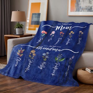 May include: Blue fleece blanket with white text that reads "First Mom Now Grandma" with floral designs and names of family members.