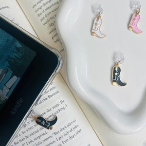May include: Three gold-tone boot charms with a star design. The boots are white, pink, and black.