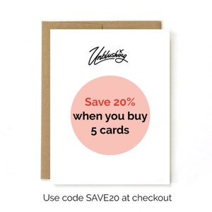 May include: A white card with a pink circle that says "Save 20% when you buy 5 cards". The text "Unblushing" is written in black cursive at the top of the card. The text "Use code SAVE20 at checkout" is written in black at the bottom of the card.