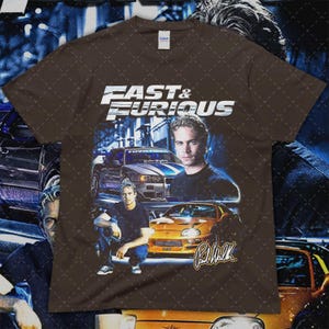 Puede incluir: Camiseta marr&oacute;n con el logo de "Fast & Furious" e im&aacute;genes de coches y Paul Walker. El dise&ntilde;o incluye un coche plateado y azul, un coche naranja y la firma de Paul Walker. La camiseta tiene cuello redondo.