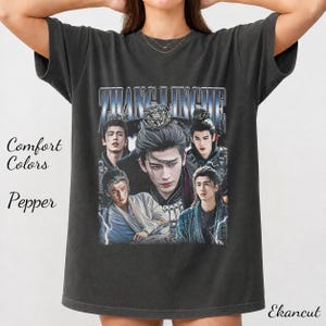 May include: A charcoal gray short-sleeve t-shirt featuring a graphic print of the actor Zhang Linghe in multiple poses. The text "ZHANG LINGHE" appears in a metallic blue font at the top. The shirt includes the printed text "Comfort Colors" and "Pepper".
