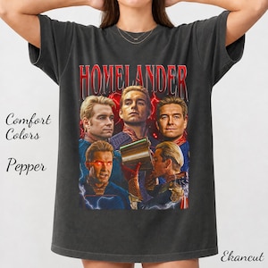 Pode incluir: Uma t-shirt cinza-carvão com uma estampa gráfica da personagem Homelander de The Boys. O design inclui vários retratos da personagem, detalhes de relâmpagos vermelhos e o texto Homelander numa fonte vermelha arrojada no topo.