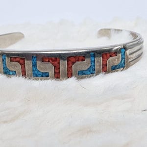 Puede incluir: Pulsera de plata con un diseño geométrico incrustado con piedras turquesa y coral.