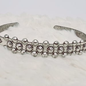 Puede incluir: Una pulsera de plata con una fila de diseños circulares decorativos en relieve.