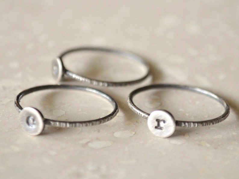 May include: Three silver rings with a textured band and a round disc with a letter stamped on it. The letters are C, R, and a third letter that is not visible.